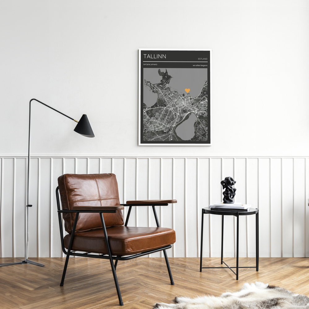 Dunkle Stadtkarte mit Herz im weißen Rahmen an einer Wand mit Wandvertäfelung neben einem braunen Ledersessel
